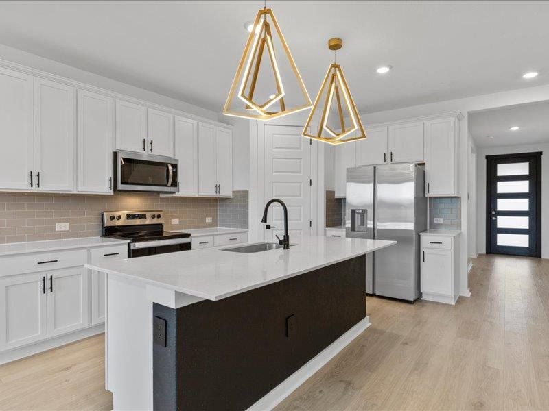 Kitchen with appliances with stainless steel finishes, white cabinetry, a center island with sink, tasteful backsplash, and light wood finished floors