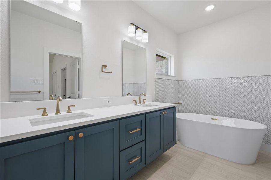 Bathroom with tile walls, tile patterned flooring, a bath, and vanity