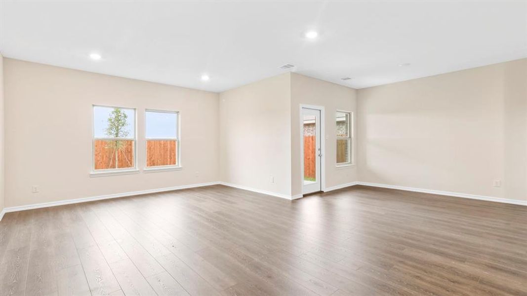 Spacious interior room featuring wood-finish flooring, recessed lighting, neutral wall tones, multiple windows, and a glass-paneled door