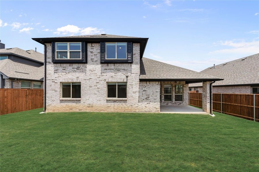 Two-story brick home rear view with covered patio, large green lawn, and wood privacy fence