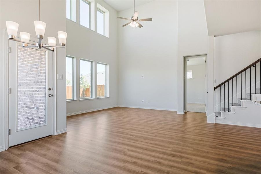 Unfurnished living room with hardwood / wood-style flooring, ceiling fan with notable chandelier, and high vaulted ceiling