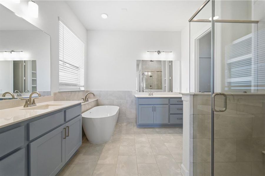 Spacious bathroom featuring dual vanities with light blue cabinetry and light-colored countertops