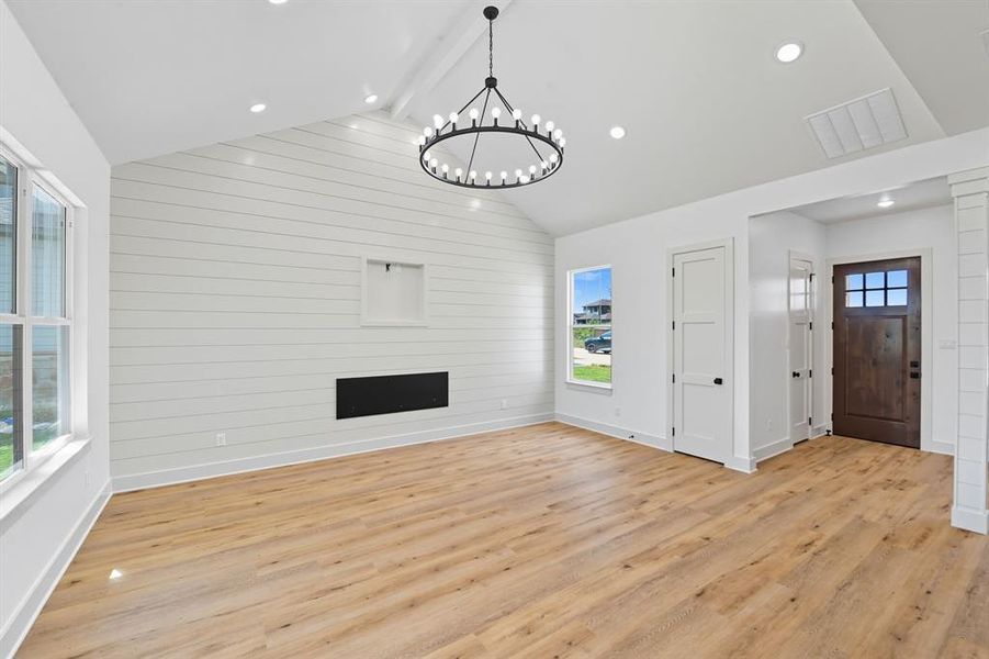 Unfurnished living room with beam ceiling, light wood-type flooring, wood walls, recessed lighting, and a chandelier Unfurnished living room with beam ceiling, light wood-type flooring, wood walls, recessed lighting, and a chandelier