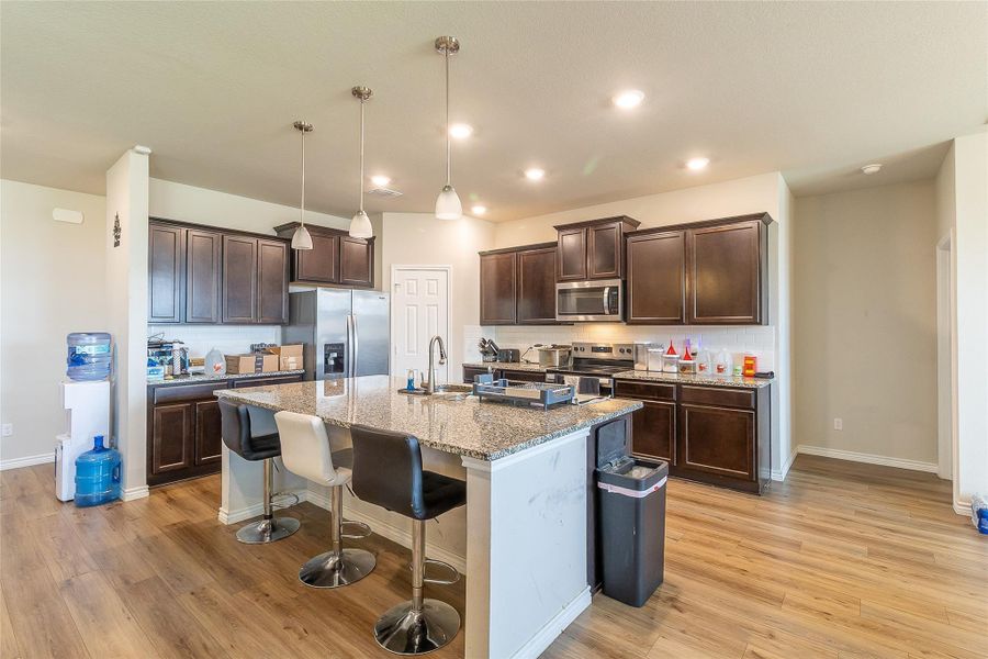 A contemporary kitchen features dark wood cabinetry, stainless steel appliances, and a spacious island with granite counters.