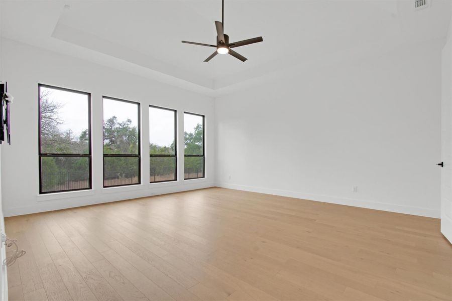 Primary Bedroom featuring a raised ceiling, light hardwood floors,  ceiling fan, and scenic, greenbelt view