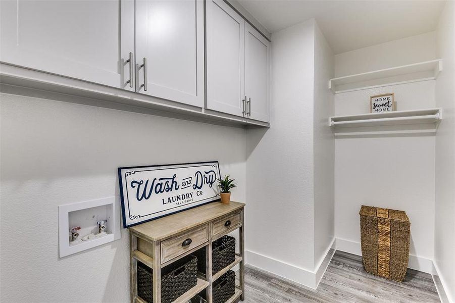 Washroom with hookup for a washing machine, cabinet space, light wood-style flooring, and baseboards