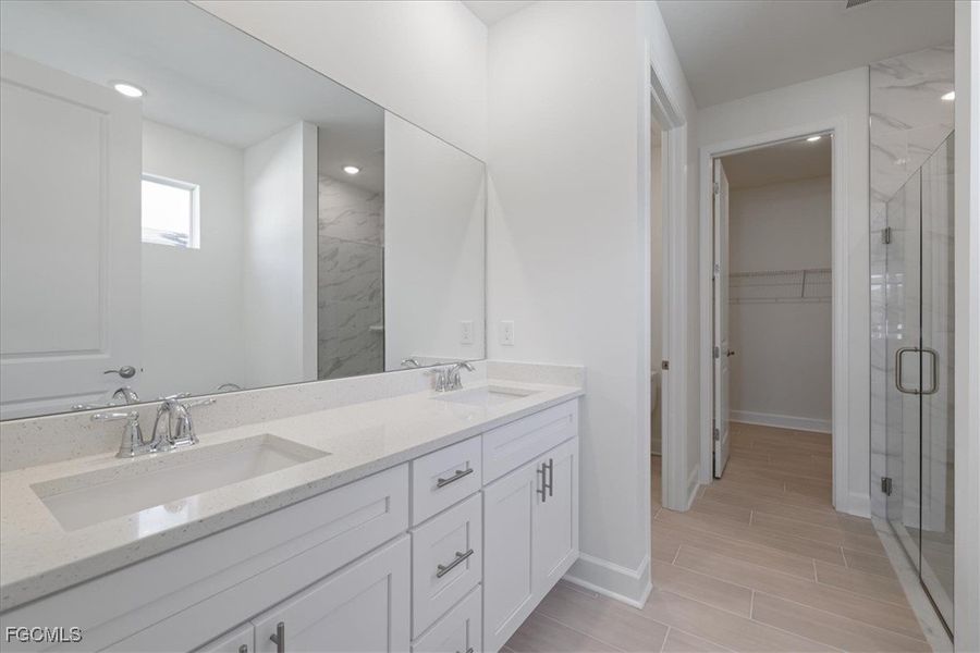 Bathroom featuring double vanity, a spacious closet, a shower stall, and wood tiled floors Bathroom featuring double vanity, a spacious closet, a shower stall, and wood tiled floors