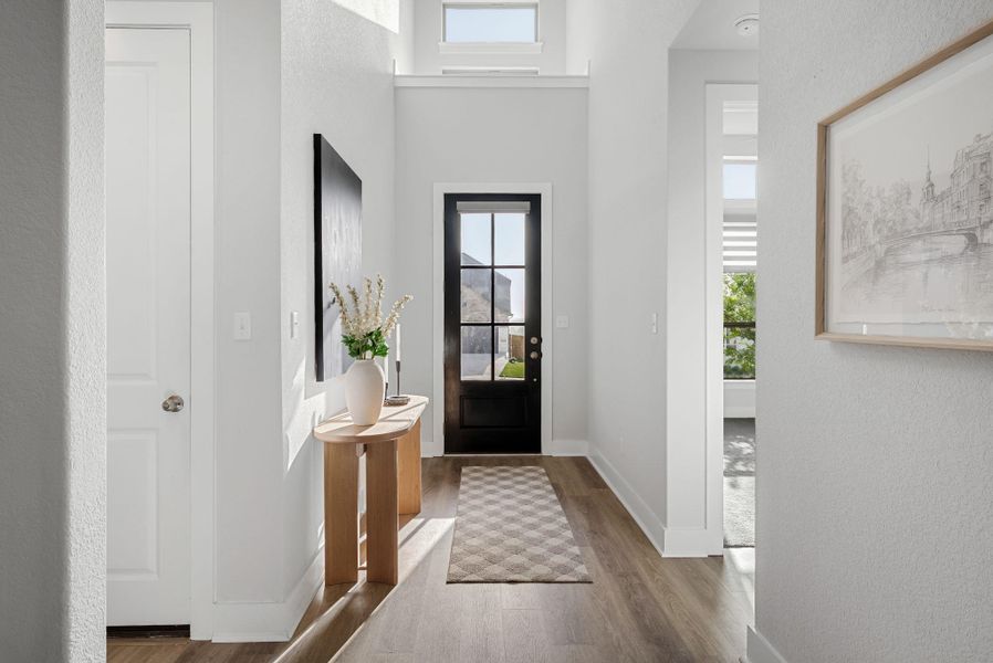 A well-lit entry hall with high ceilings, showcasing elegant wood flooring and a classic paneled front door.