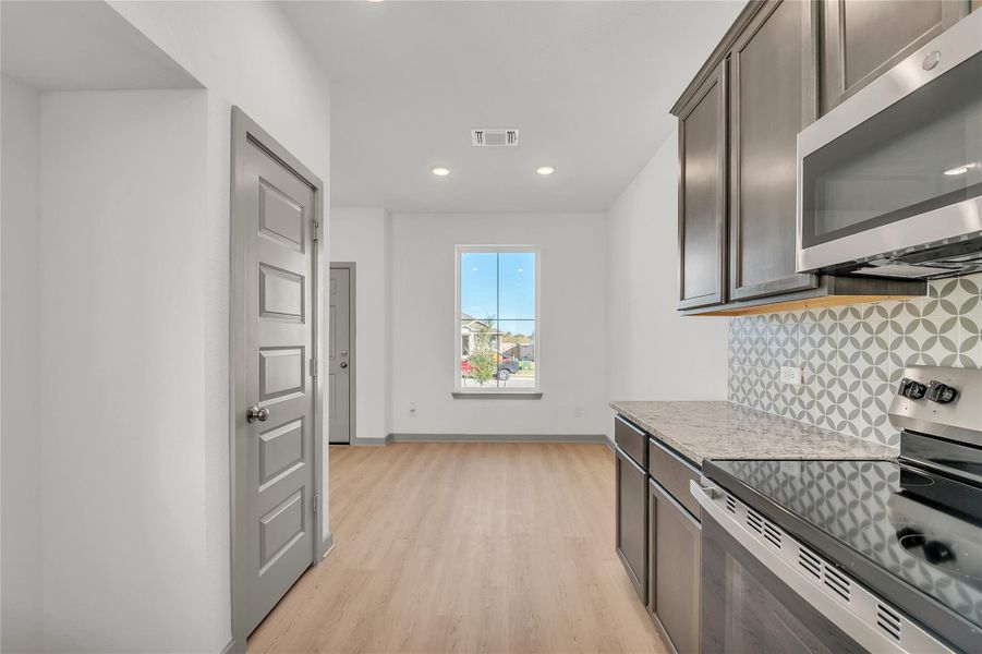 Kitchen with stainless steel appliances, light stone countertops, light wood finished floors, backsplash, and dark wood finish cabinets