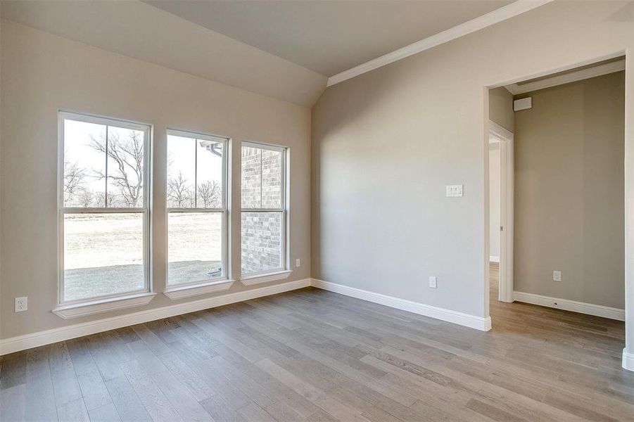 Spare room with lofted ceiling, ornamental molding, and light wood-type flooring