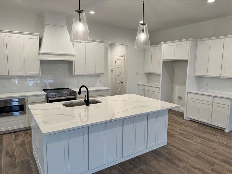 Kitchen with hanging light fixtures, sink, range with electric stovetop, and a kitchen island with sink