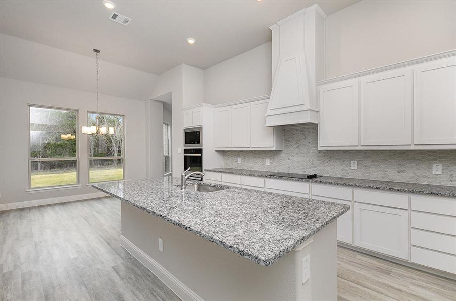 Kitchen with wall oven, white cabinetry, sink, and an island with sink