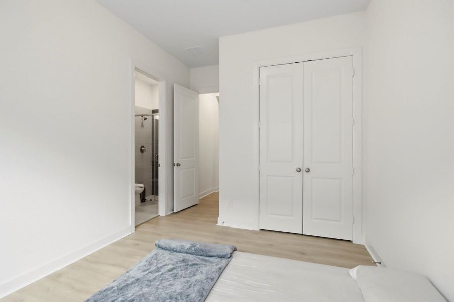 Bright bedroom with sleek wood flooring, a spacious closet, and an ensuite bathroom.