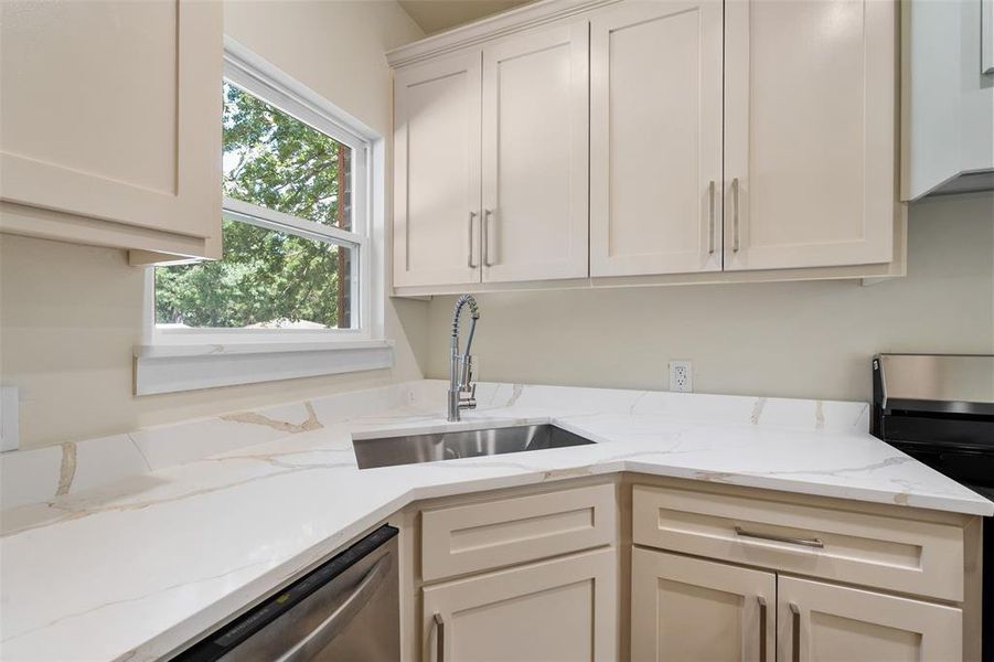 Contemporary kitchen featuring light-toned cabinetry, stainless steel sink with a high-arc faucet, white countertops with veining, and a double-hung window Contemporary kitchen featuring light-toned cabinetry, stainless steel sink with a high-arc faucet, white countertops with veining, and a double-hung window