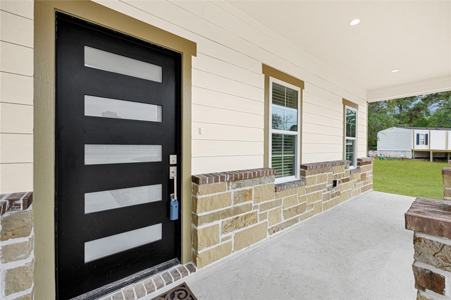 This photo showcases a welcoming front porch with a modern black door featuring frosted glass panels. The exterior combines brick and siding, and the porch overlooks a spacious yard with greenery. This photo showcases a welcoming front porch with a modern black door featuring frosted glass panels. The exterior combines brick and siding, and the porch overlooks a spacious yard with greenery.