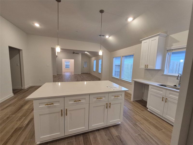 Spacious open-concept kitchen and living area featuring modern pendant lighting, sleek white cabinetry, and elegant wood-look flooring for a contemporary feel.
