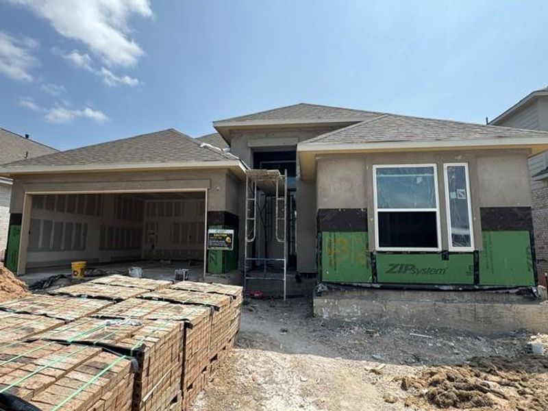 Under-construction facade with an open garage and initial window installations, presenting a home in progress.