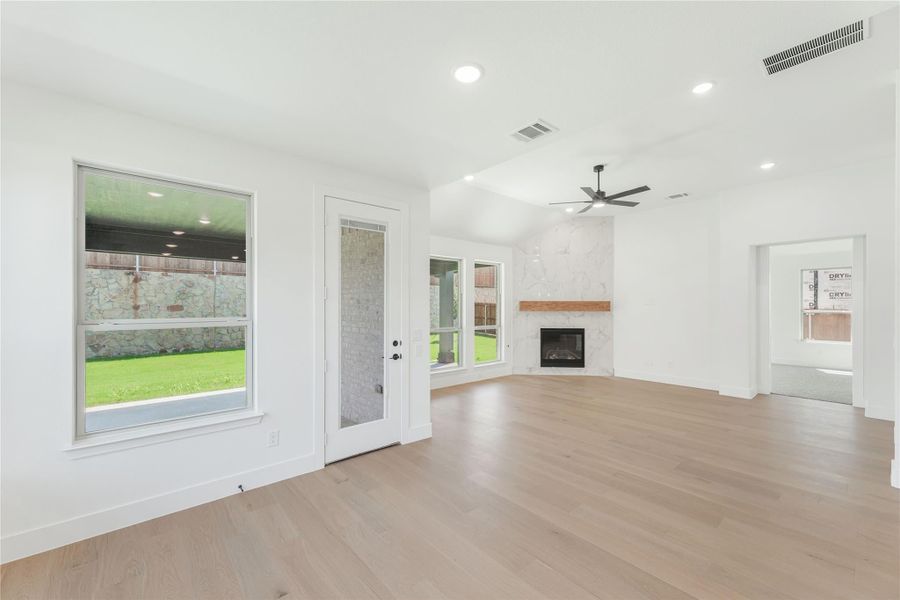 Open living room with light wood floors, marble fireplace, ceiling fan, and glass back door Open living room with light wood floors, marble fireplace, ceiling fan, and glass back door
