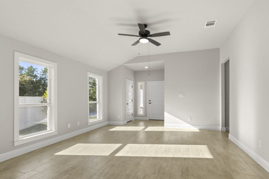 Image of a one story home living room with light wood-like flooring and light grey painted walls with two large windows and a ceiling fan Image of a one story home living room with light wood-like flooring and light grey painted walls with two large windows and a ceiling fan