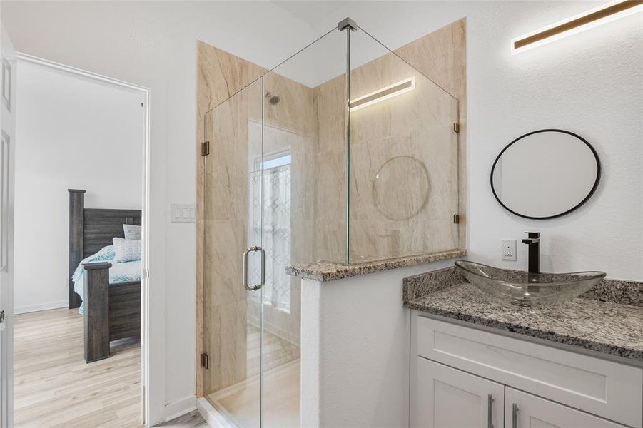 Another view of the primary bathroom with a  sleek vessel sink atop a granite countertop, and contemporary lighting.