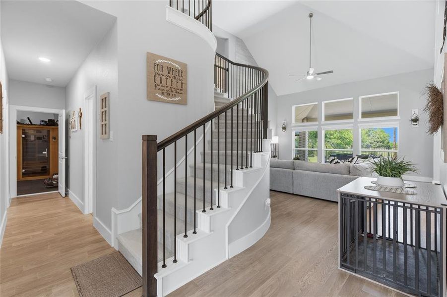 Curved staircase with dark wood handrail and black iron balusters, light wood-finish flooring, and high vaulted ceilings