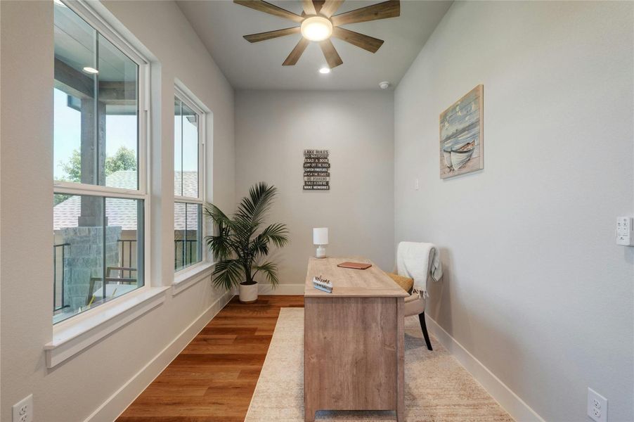 Dedicated room featuring abundant natural light, wood-finish flooring, a contemporary ceiling fan with integrated lighting, and neutral wall tones