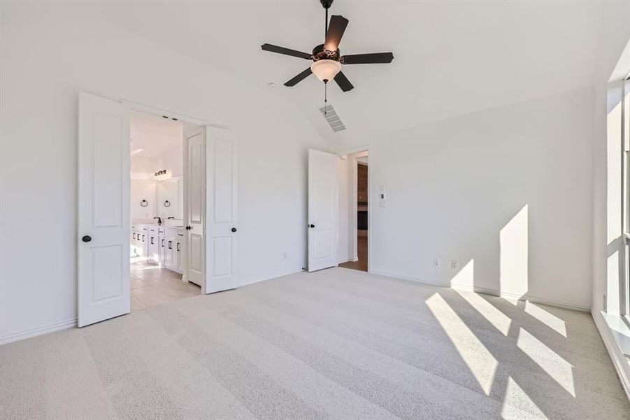 Unfurnished bedroom with connected bathroom, lofted ceiling, light carpet, and ceiling fan