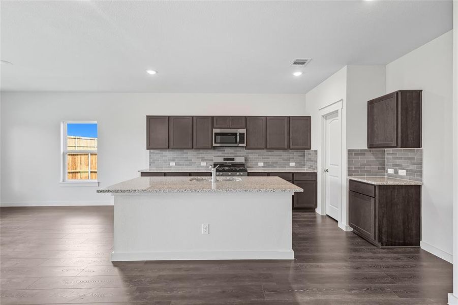 Kitchen featuring decorative backsplash, dark brown cabinetry, light stone counters, stainless steel appliances, and dark wood-style flooring Kitchen featuring decorative backsplash, dark brown cabinetry, light stone counters, stainless steel appliances, and dark wood-style flooring