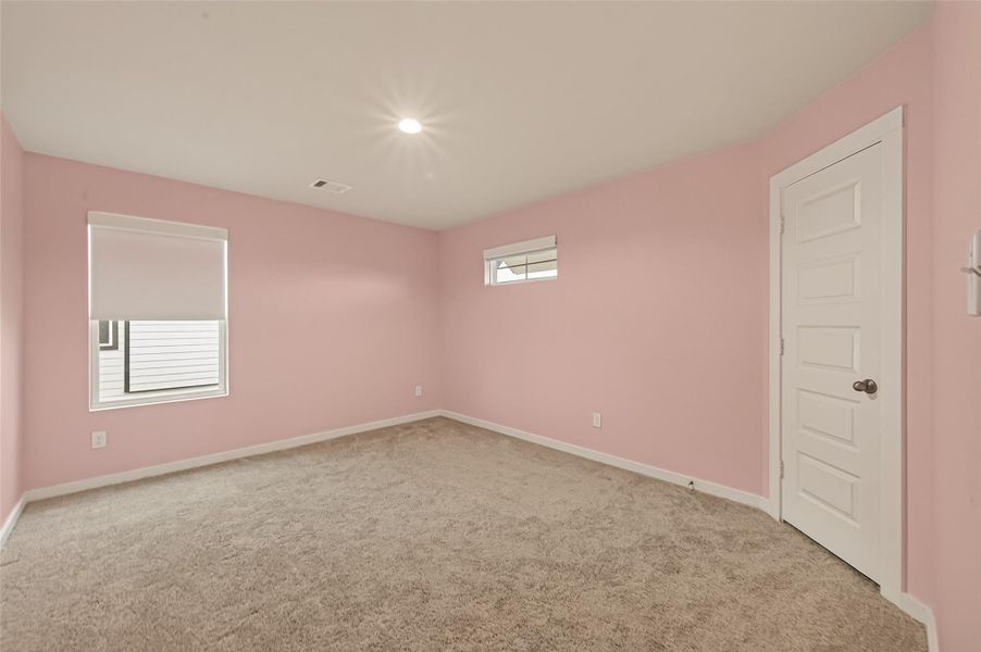 The secondary bedroom on the second floor features pink blush walls, carpeted flooring, and a window that lets in natural light.