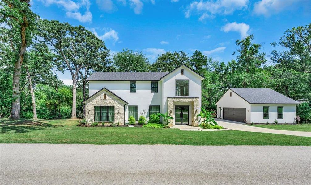 View of front of house featuring stone siding, a garage, a front yard, stucco siding, and an outbuilding View of front of house featuring stone siding, a garage, a front yard, stucco siding, and an outbuilding