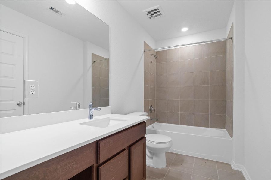 The secondary bathroom showcases tile flooring, a bath/shower combo with Daltile tile surround, a vanity with knee space and stunning light countertop, a stylish mirror, sleek fixtures, and contemporary finishes throughout. The secondary bathroom showcases tile flooring, a bath/shower combo with Daltile tile surround, a vanity with knee space and stunning light countertop, a stylish mirror, sleek fixtures, and contemporary finishes throughout.