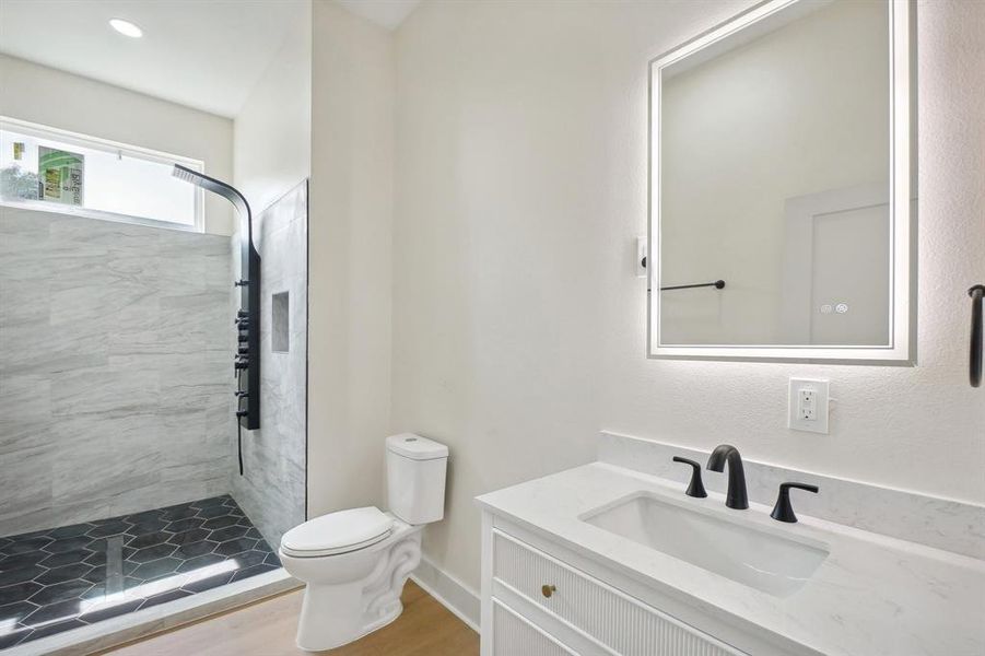 Bathroom featuring wood-type flooring, vanity, toilet, and tiled shower