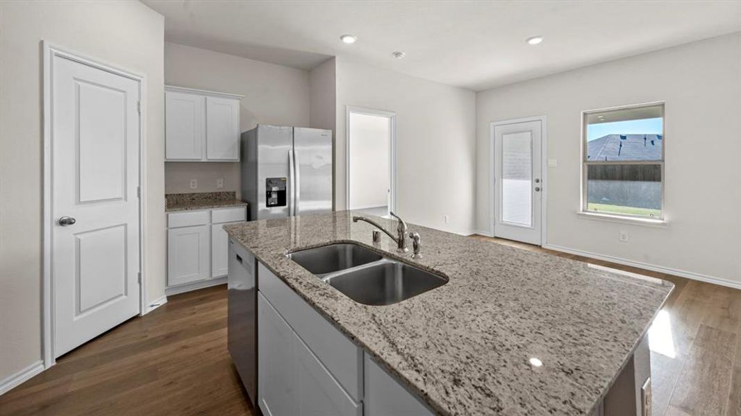 Kitchen featuring stainless steel appliances, an island with sink, dark wood-type flooring, light stone counters, and recessed lighting