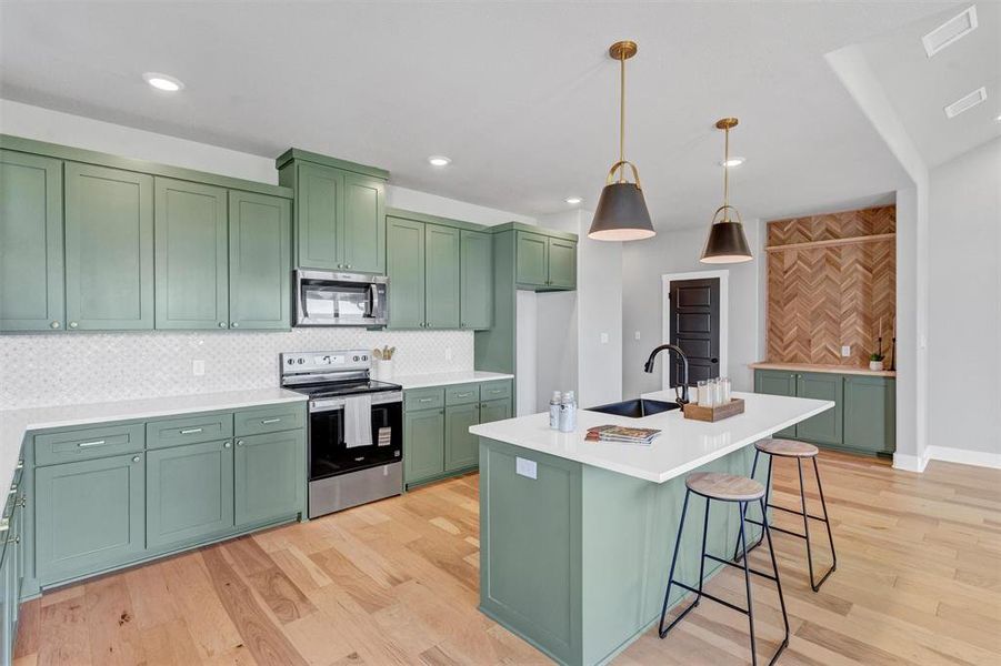 Kitchen with green cabinetry, stainless steel appliances, decorative backsplash, light wood-style flooring, and hanging light fixtures Kitchen with green cabinetry, stainless steel appliances, decorative backsplash, light wood-style flooring, and hanging light fixtures