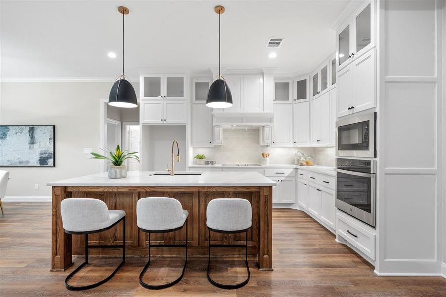 Kitchen with oven, a sink, built in microwave, visible vents, and a center island with sink