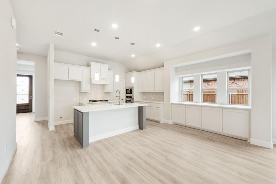 Open kitchen with white cabinets, center island, pendant lights, and light wood floors