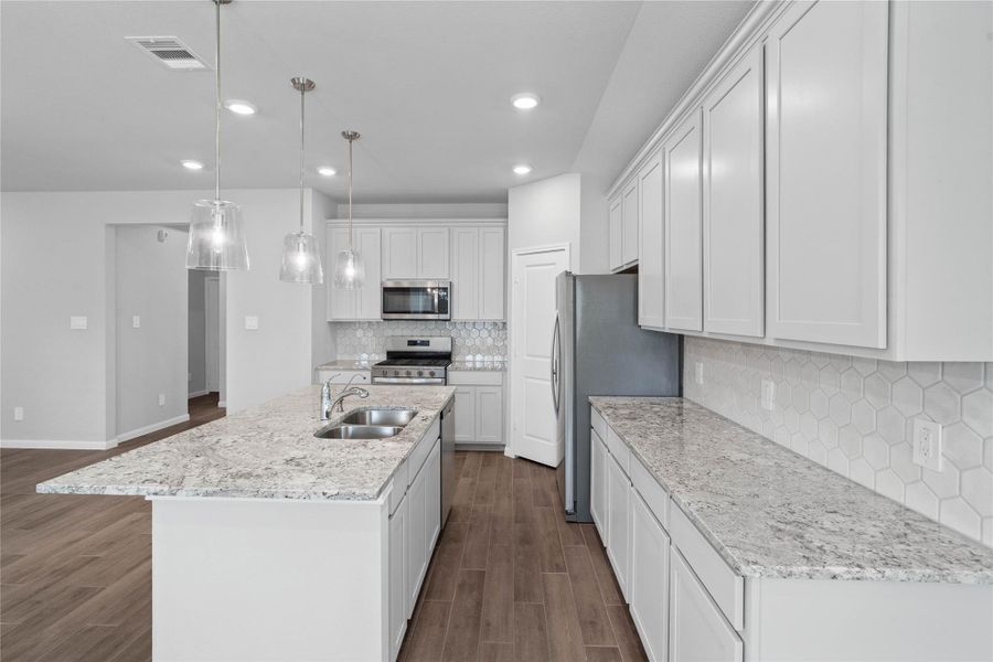 Discover this chef-ready kitchen featuring sleek, shaker-style white cabinetry, Andino White granite countertops, and a full suite of stainless steel appliances, including an over-the-range microwave and a side-by-side refrigerator.