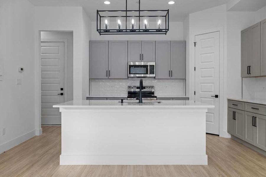 Kitchen featuring gray cabinetry, tasteful backsplash, light stone countertops, an island with sink, and recessed lighting Kitchen featuring gray cabinetry, tasteful backsplash, light stone countertops, an island with sink, and recessed lighting