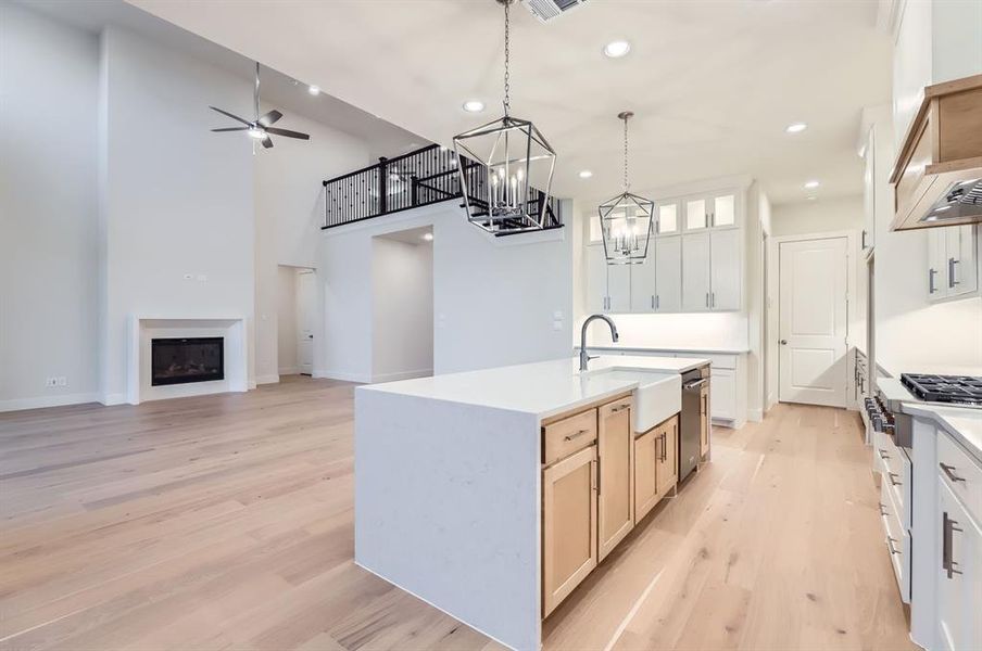 Kitchen with a kitchen island with sink, ceiling fan with notable chandelier, sink, light hardwood / wood-style floors, and white cabinetry