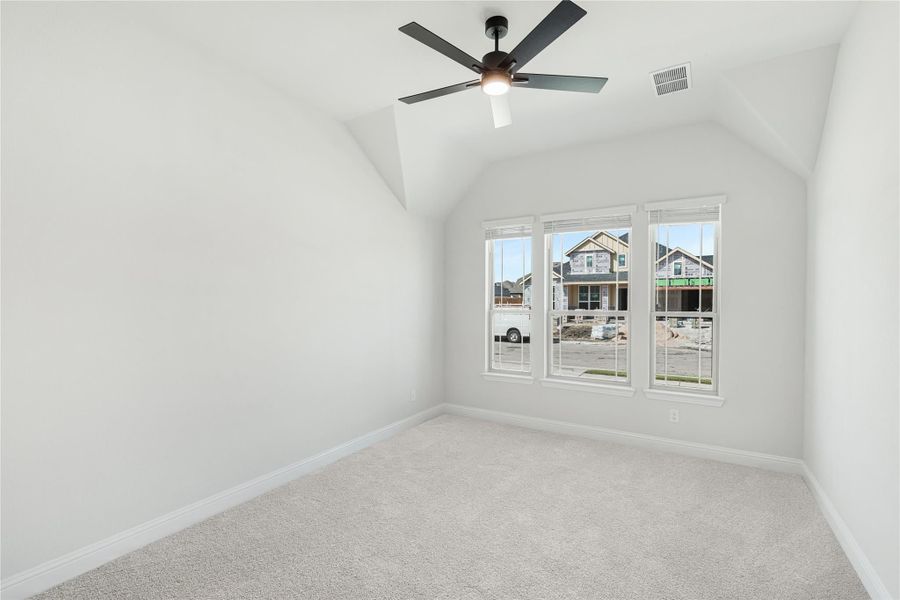 Empty bedroom with vaulted ceiling, ceiling fan, carpet flooring, and triple window overlooking new construction