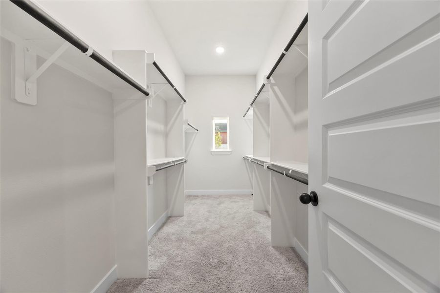 This is a spacious walk-in closet with ample hanging space, shelving, and carpeted flooring found in the downstairs primary bedroom. A small window provides natural light, creating a bright and inviting atmosphere. This is a spacious walk-in closet with ample hanging space, shelving, and carpeted flooring found in the downstairs primary bedroom. A small window provides natural light, creating a bright and inviting atmosphere.