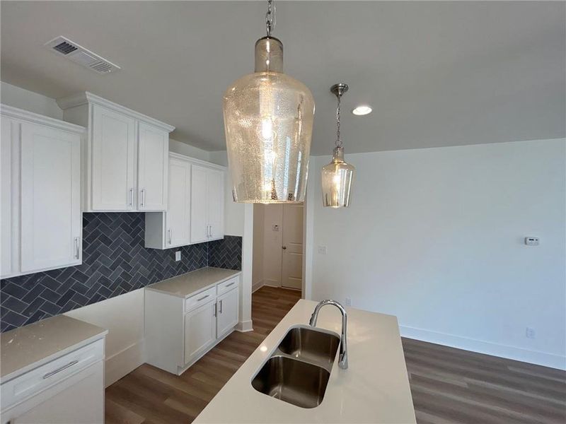 Kitchen featuring dark hardwood / wood-style flooring, sink, hanging light fixtures, tasteful backsplash, and white cabinetry