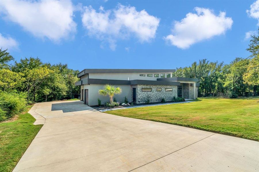 View of front of home featuring concrete driveway, stucco siding, a front yard, stone siding, and view of wooded area