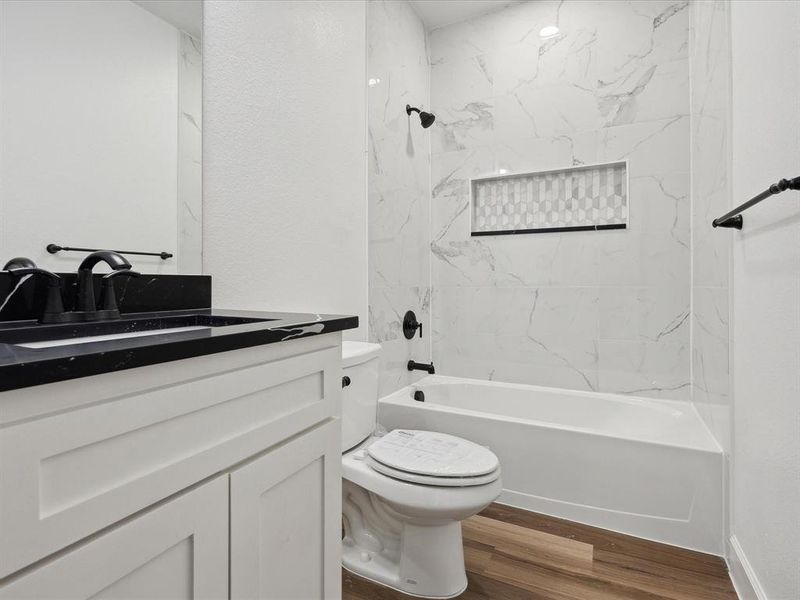 Full bathroom featuring vanity, tiled shower / bath combo, hardwood / wood-style flooring, and toilet