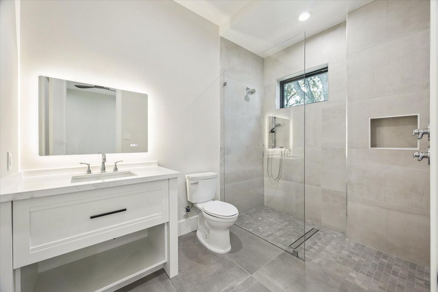 A quartz-topped vanity with undermount sink and lighted mirror sets the tone for modern style. The walk-in shower with soap inset completes the spa-like feel.
