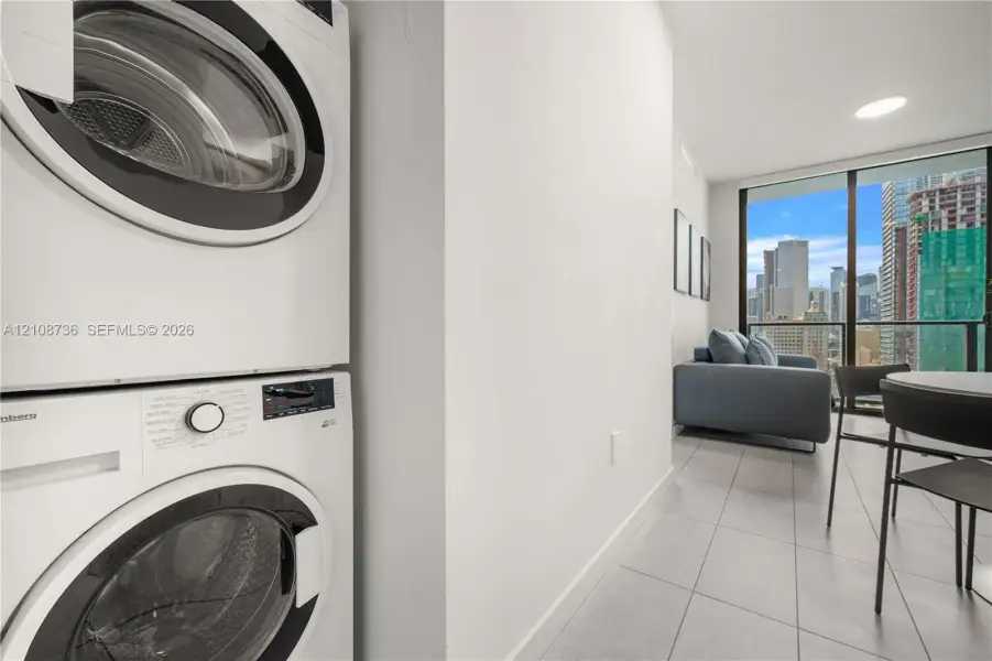 Stacked white front-load laundry unit, floor-to-ceiling windows, and tile flooring Stacked white front-load laundry unit, floor-to-ceiling windows, and tile flooring