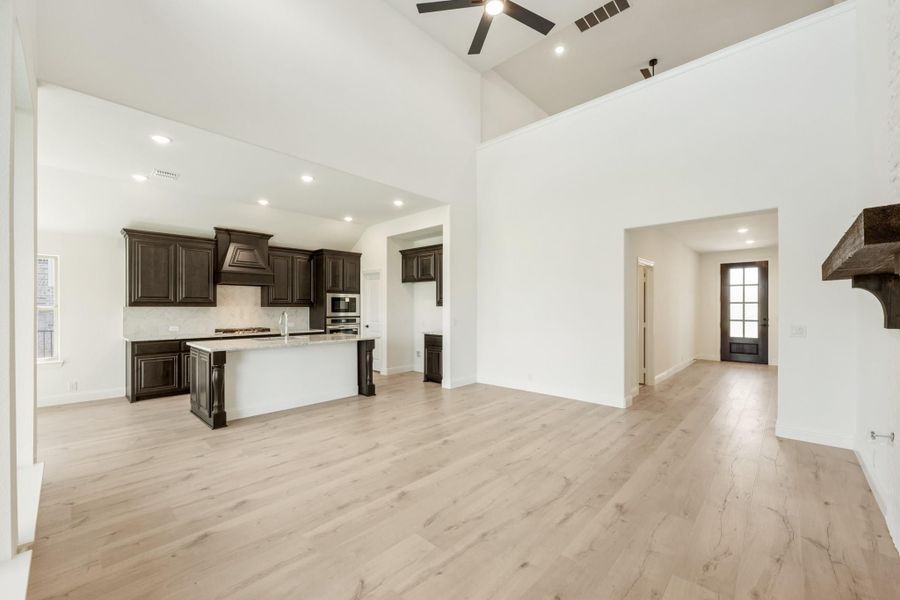 Open living area with kitchen island, dark cabinets, vaulted ceiling, ceiling fan, and light wood floors