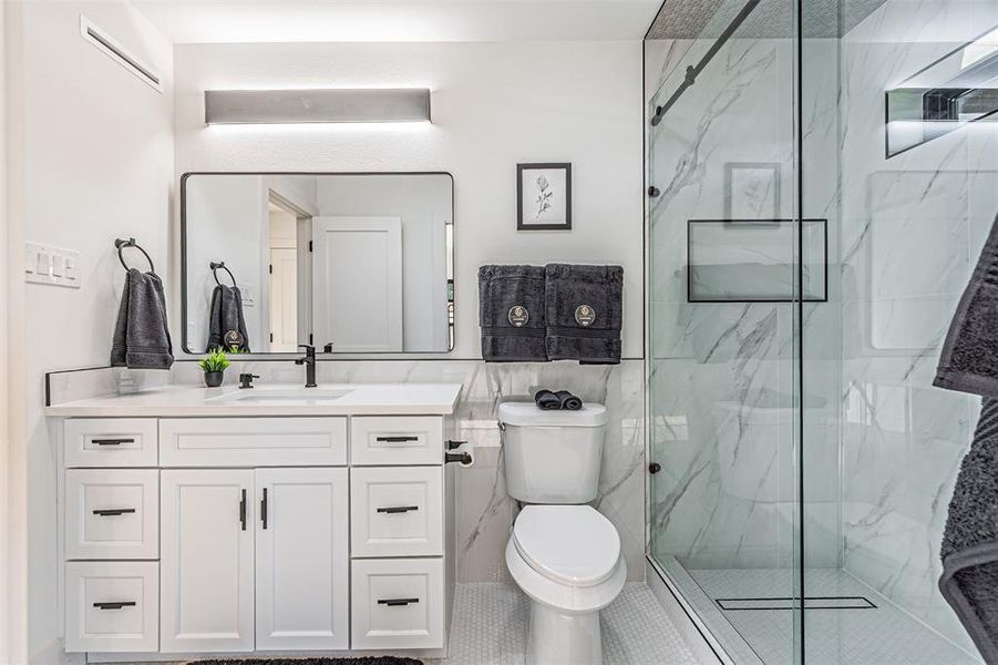 Bathroom featuring vanity, a marble finish shower, tile walls, and tile patterned flooring