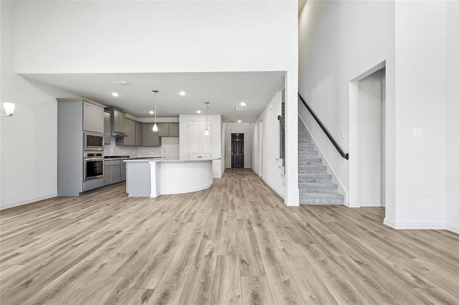 Kitchen with gray cabinets, appliances with stainless steel finishes, open floor plan, wall chimney range hood, and light wood-type flooring Kitchen with gray cabinets, appliances with stainless steel finishes, open floor plan, wall chimney range hood, and light wood-type flooring