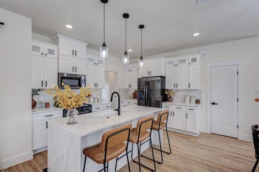 Kitchen with glass insert cabinets, a kitchen breakfast bar, light stone countertops, white cabinets, and recessed lighting Kitchen with glass insert cabinets, a kitchen breakfast bar, light stone countertops, white cabinets, and recessed lighting